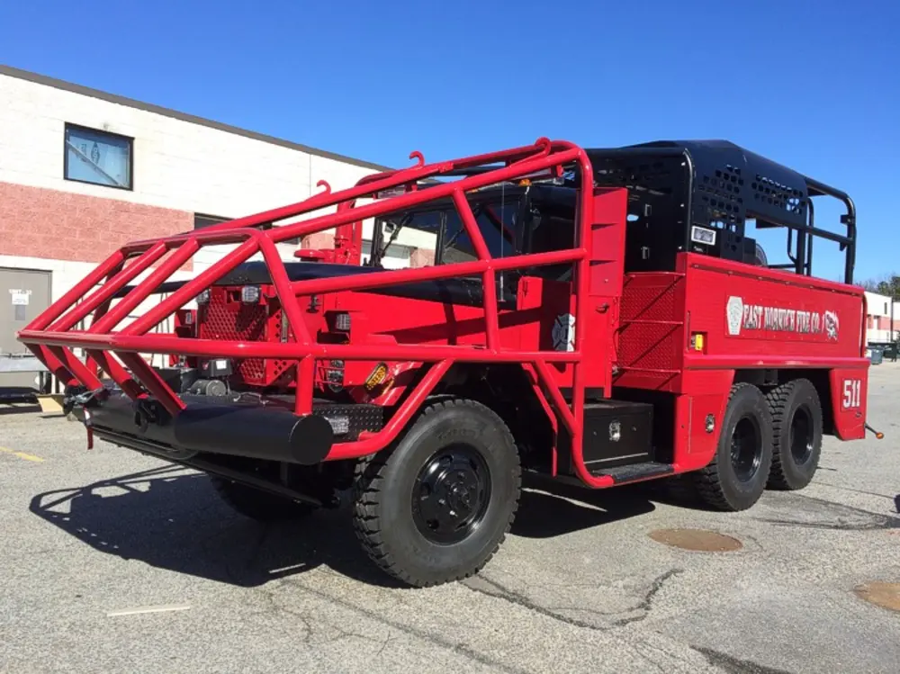 Exterior view of small fire truck showing cab, body compartments, and wheel/tire area.