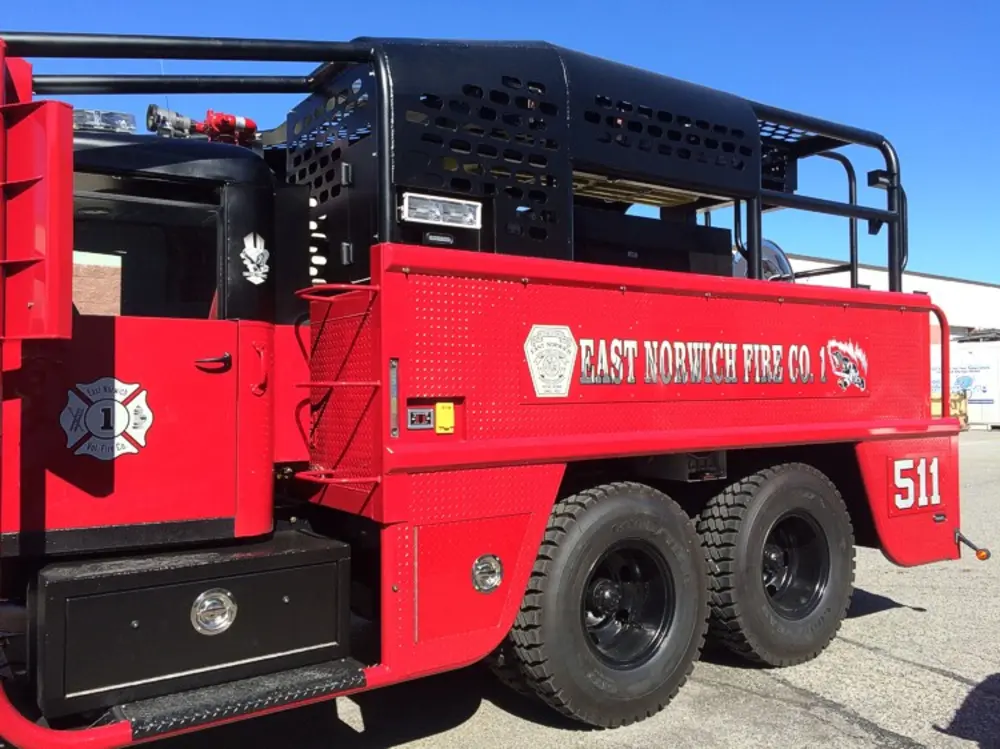 Exterior view of small fire truck showing cab, body compartments, and wheel/tire area.
