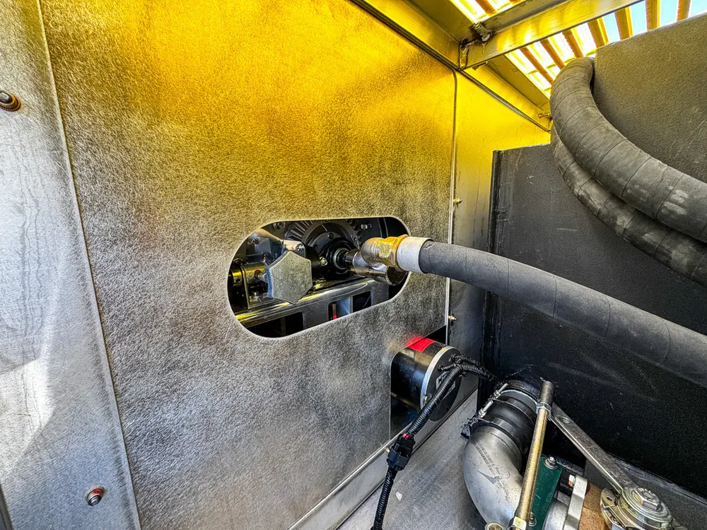 Compartment wall close-up with hose passing through a grommeted opening.