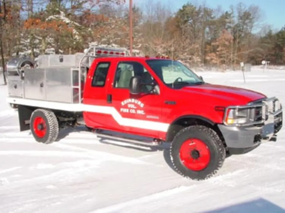 Exterior view of small fire truck showing cab, body compartments, and wheel/tire area.