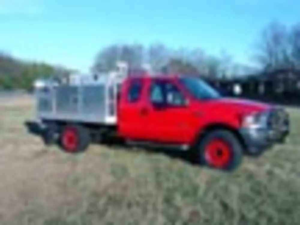 Exterior view of small fire truck showing cab, body compartments, and wheel/tire area.