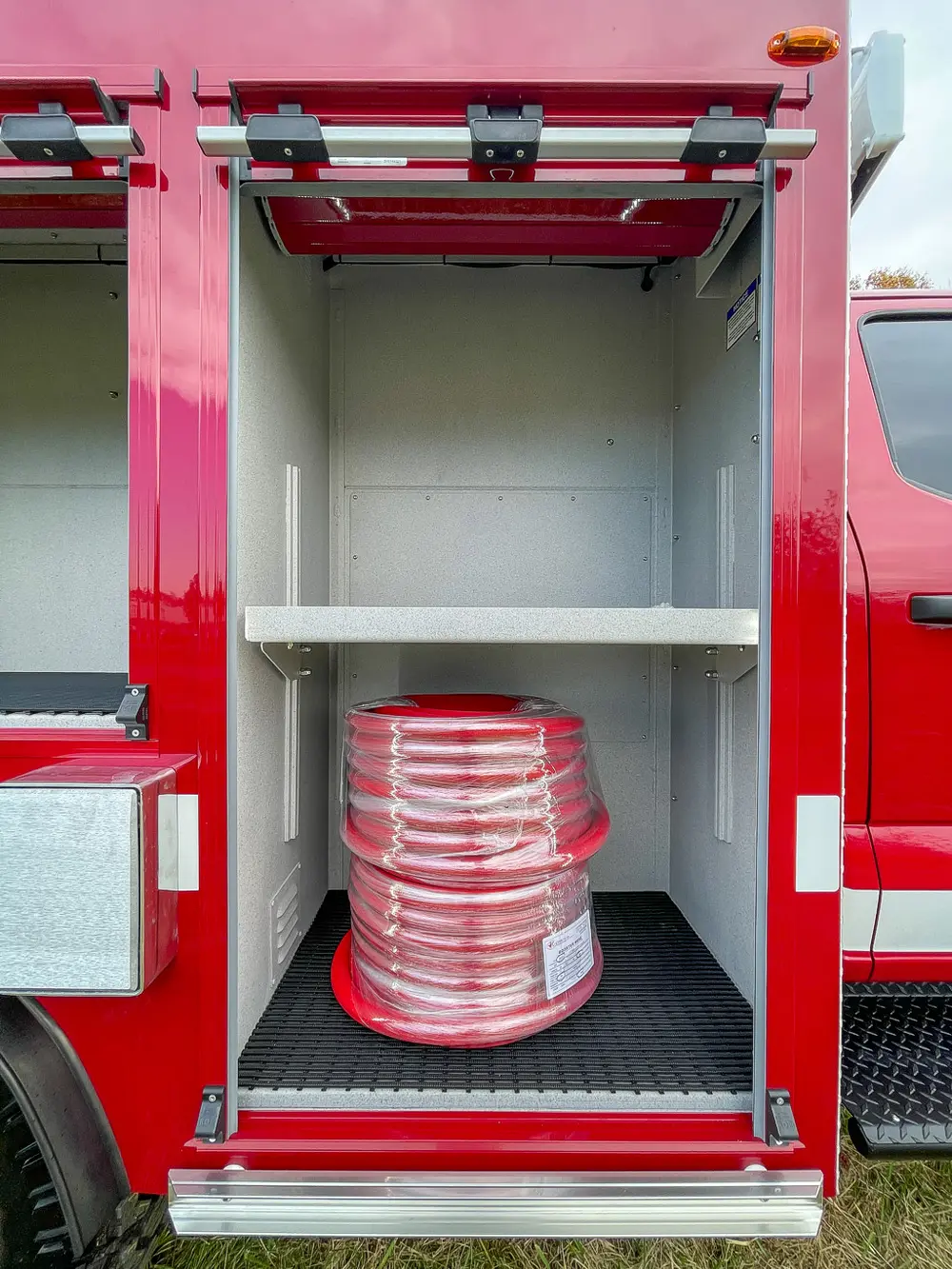 Compartment shelf with coiled red hose stored at lower right.
