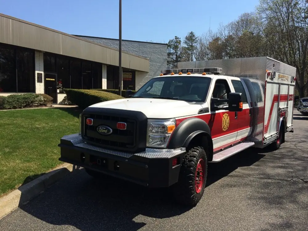 Exterior view of small fire truck showing cab, body compartments, and wheel/tire area.