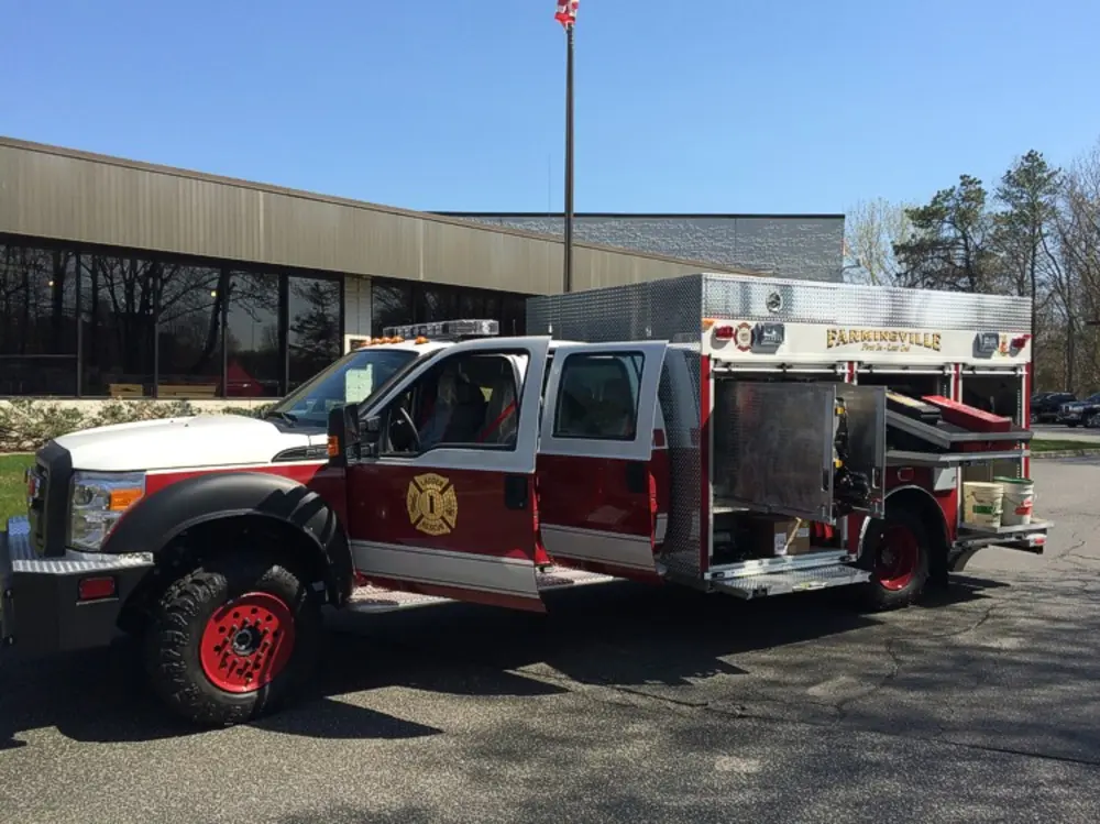 Exterior view of small fire truck showing cab, body compartments, and wheel/tire area.