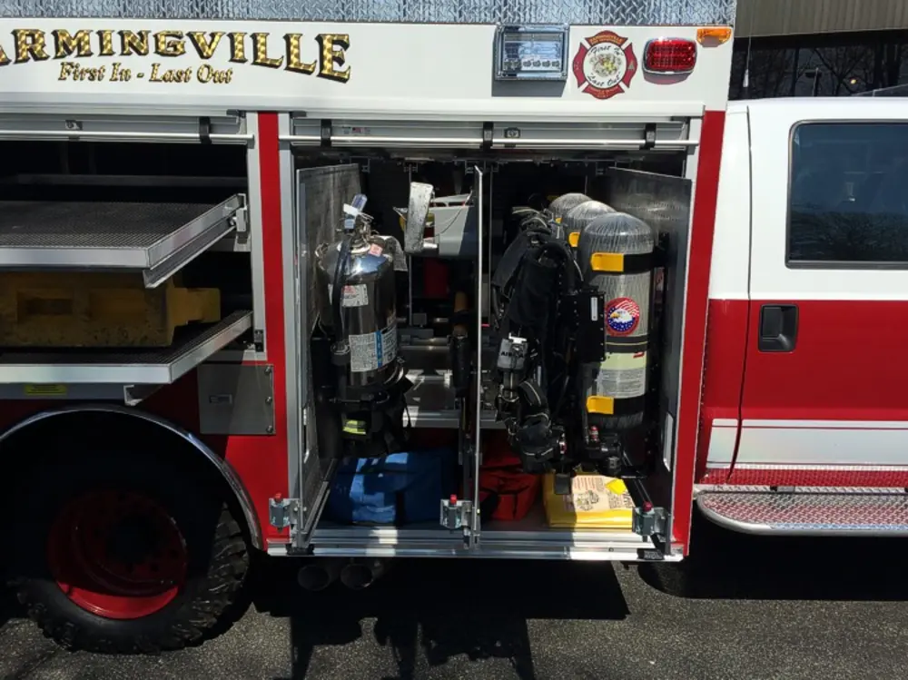 Exterior view of small fire truck showing cab, body compartments, and wheel/tire area.