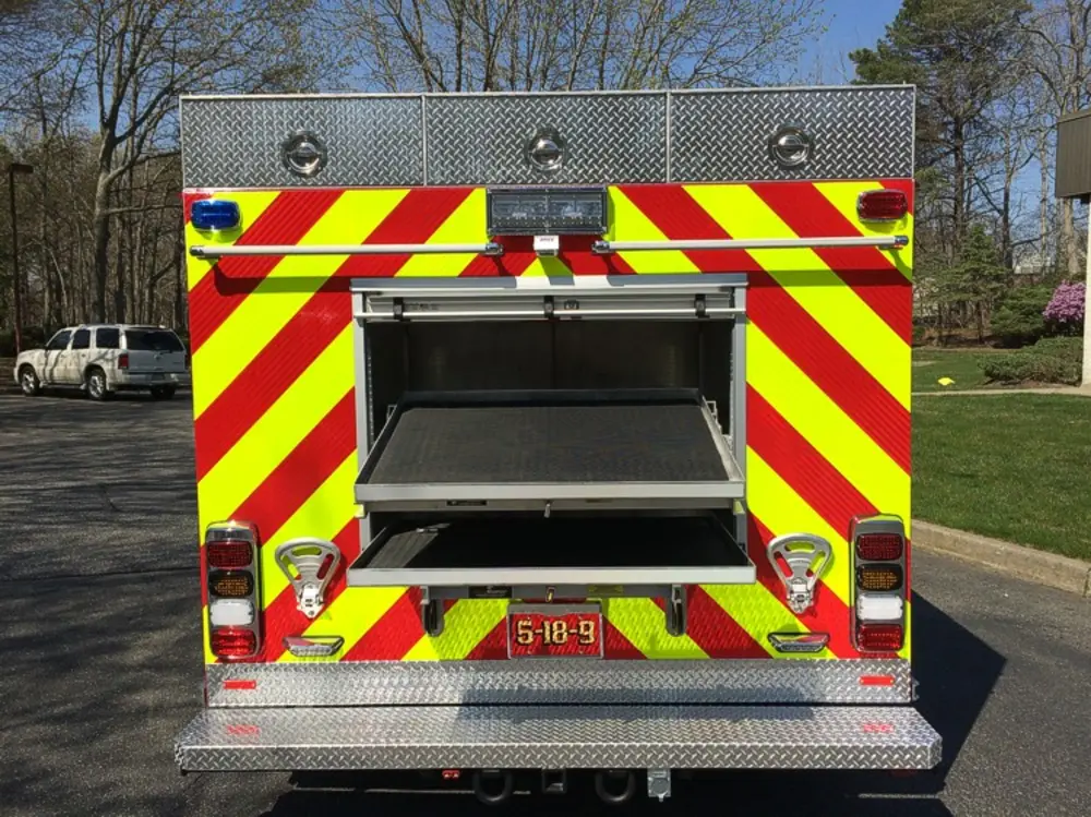 Exterior view of small fire truck showing cab, body compartments, and wheel/tire area.
