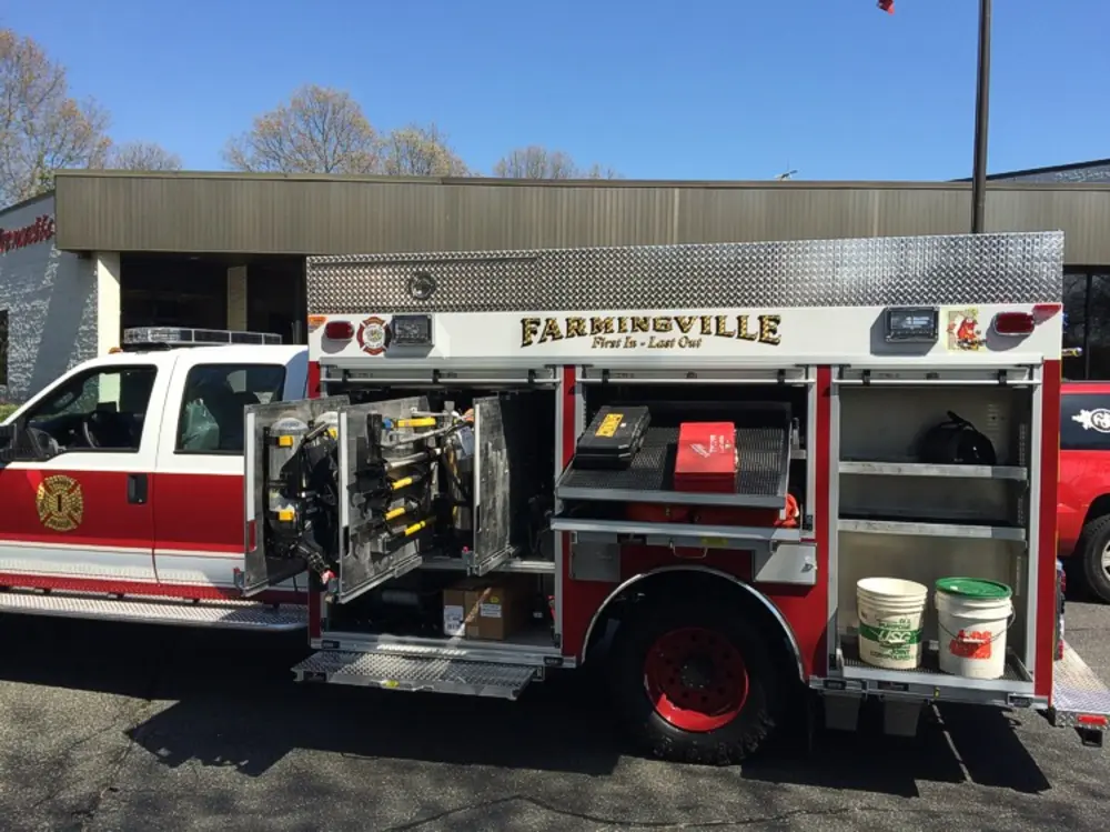 Exterior view of small fire truck showing cab, body compartments, and wheel/tire area.