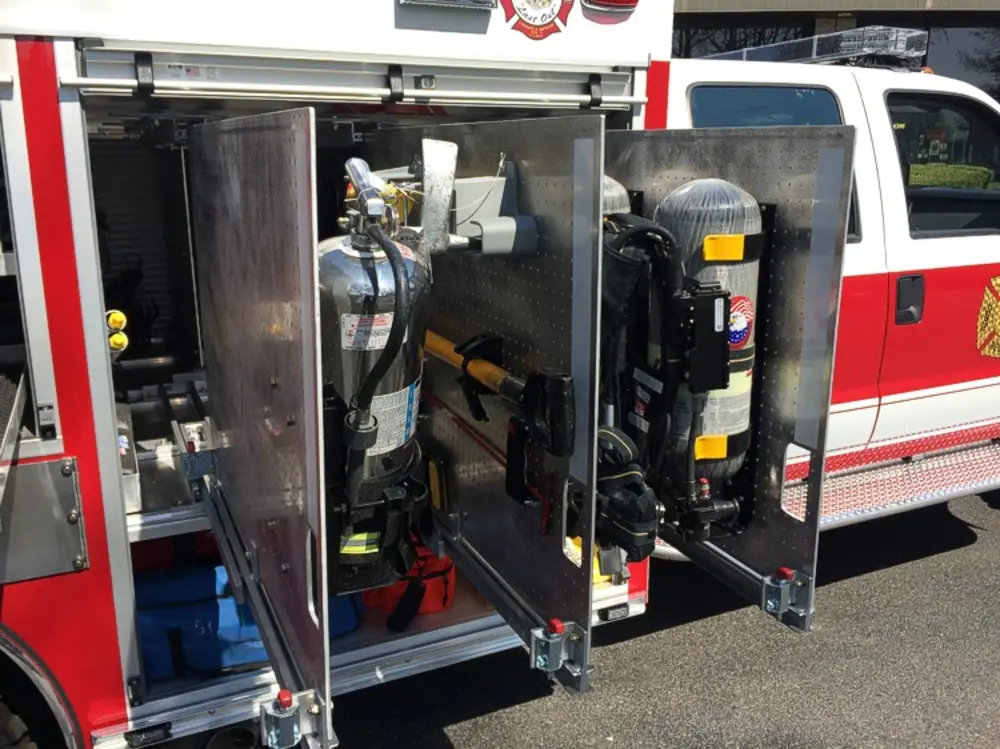 Exterior view of small fire truck showing cab, body compartments, and wheel/tire area.