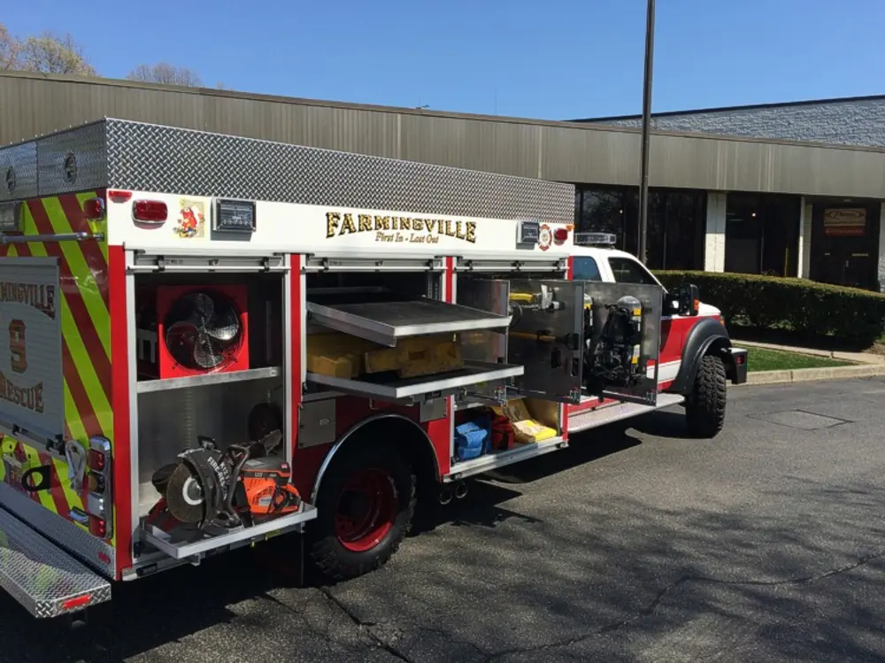 Exterior view of small fire truck showing cab, body compartments, and wheel/tire area.