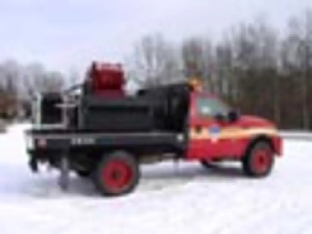 Exterior view of small fire truck showing cab, body compartments, and wheel/tire area.