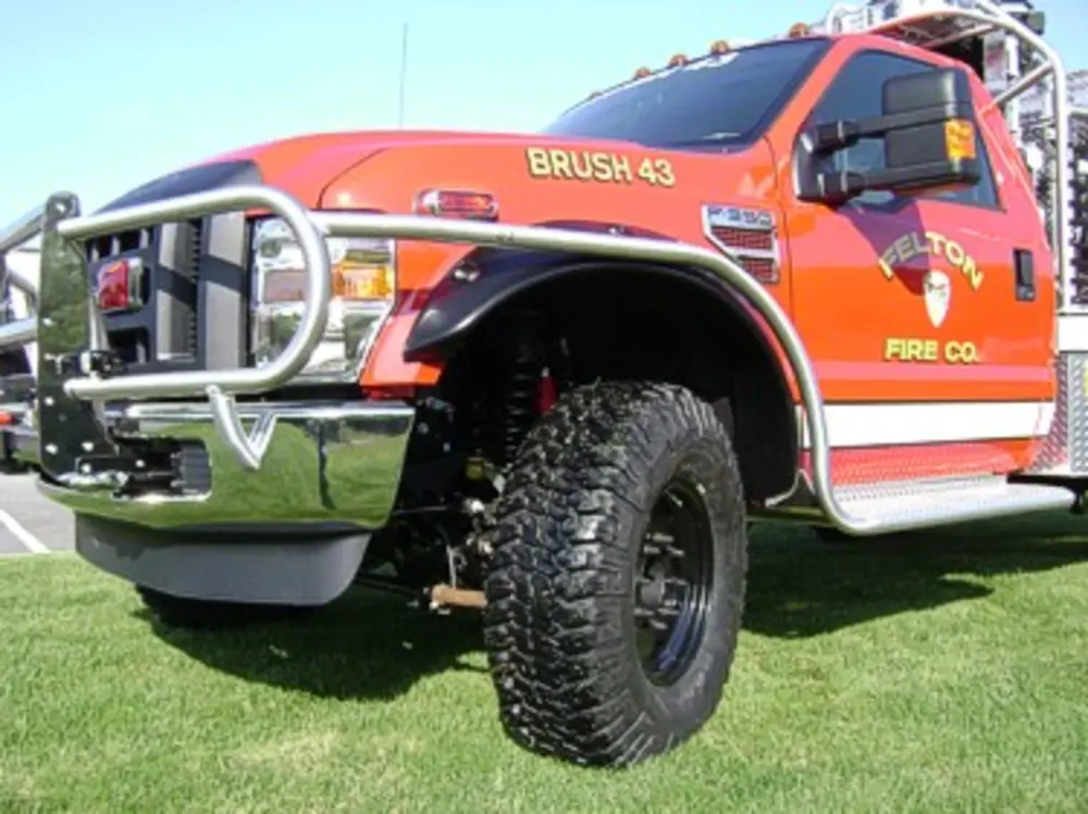 Exterior view of small fire truck showing cab, body compartments, and wheel/tire area.