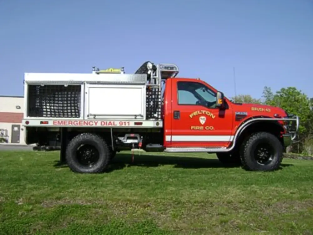 Exterior view of small fire truck showing cab, body compartments, and wheel/tire area.