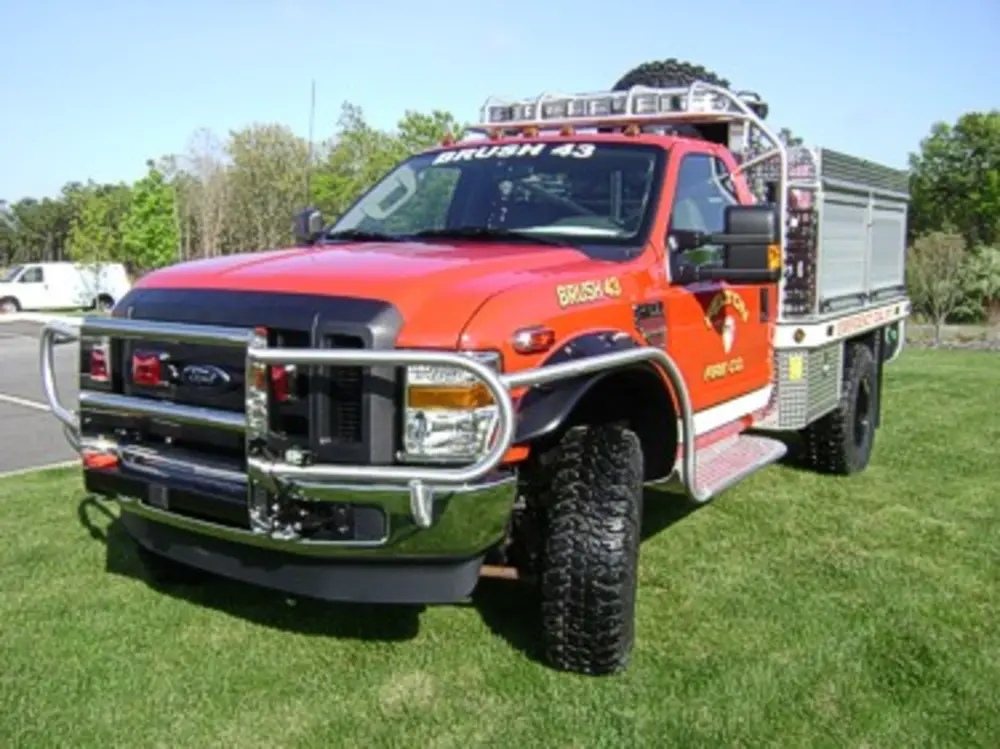 Exterior view of small fire truck showing cab, body compartments, and wheel/tire area.