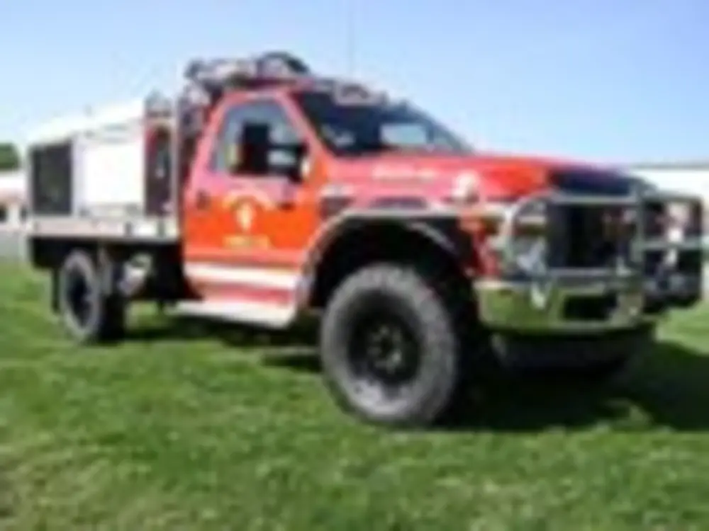 Exterior view of small fire truck showing cab, body compartments, and wheel/tire area.