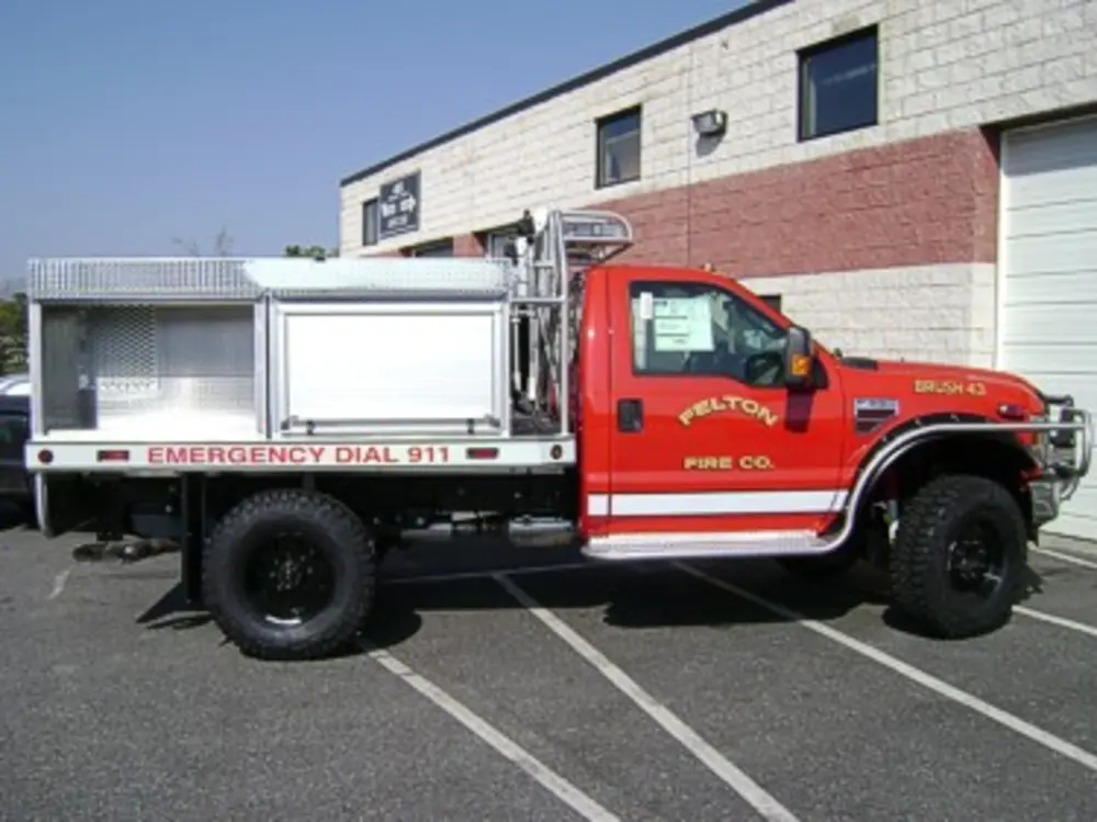 Exterior view of small fire truck showing cab, body compartments, and wheel/tire area.