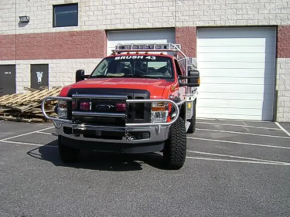 Exterior view of small fire truck showing cab, body compartments, and wheel/tire area.