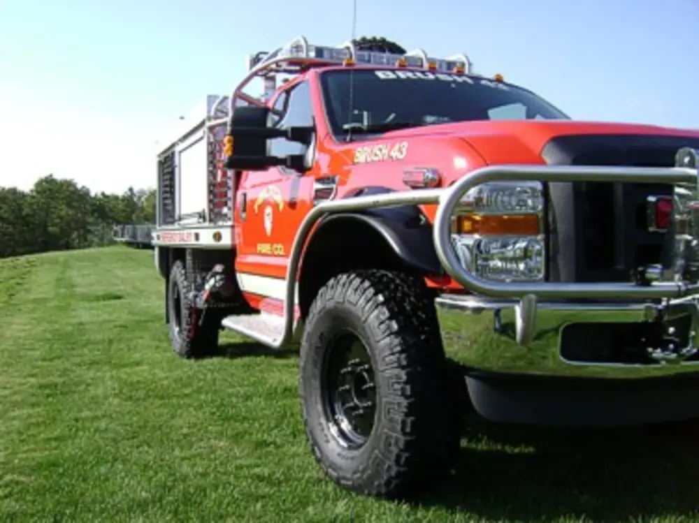 Exterior view of small fire truck showing cab, body compartments, and wheel/tire area.