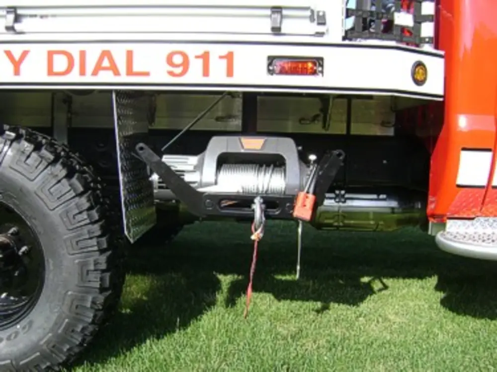 Exterior view of small fire truck showing cab, body compartments, and wheel/tire area.