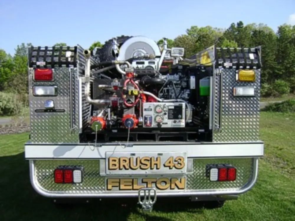 Exterior view of small fire truck showing cab, body compartments, and wheel/tire area.