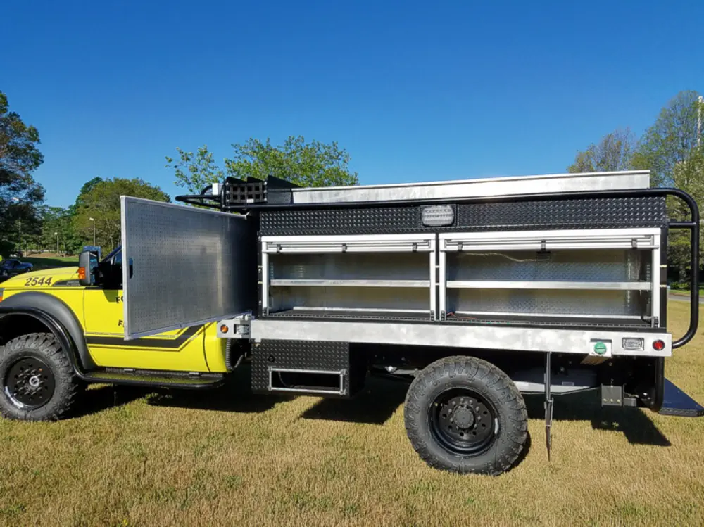 Exterior view of small fire truck showing cab, body compartments, and wheel/tire area.