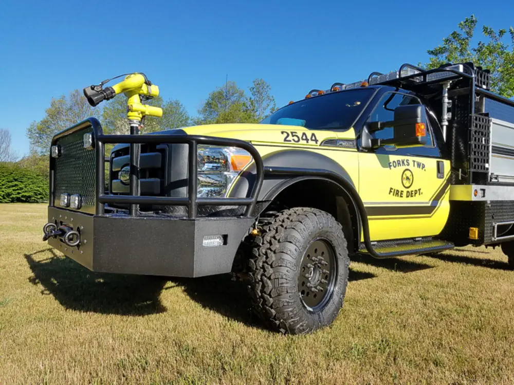 Exterior view of small fire truck showing cab, body compartments, and wheel/tire area.