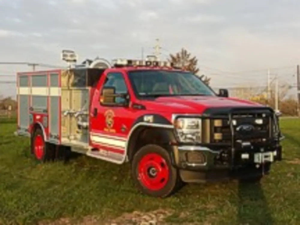 Exterior view of small fire truck showing cab, body compartments, and wheel/tire area.