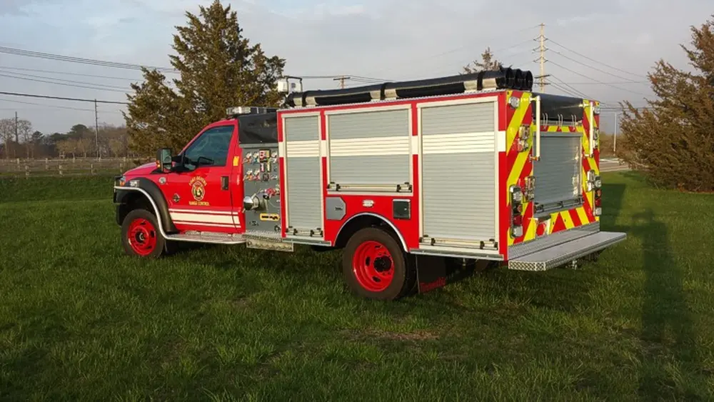 Exterior view of small fire truck showing cab, body compartments, and wheel/tire area.