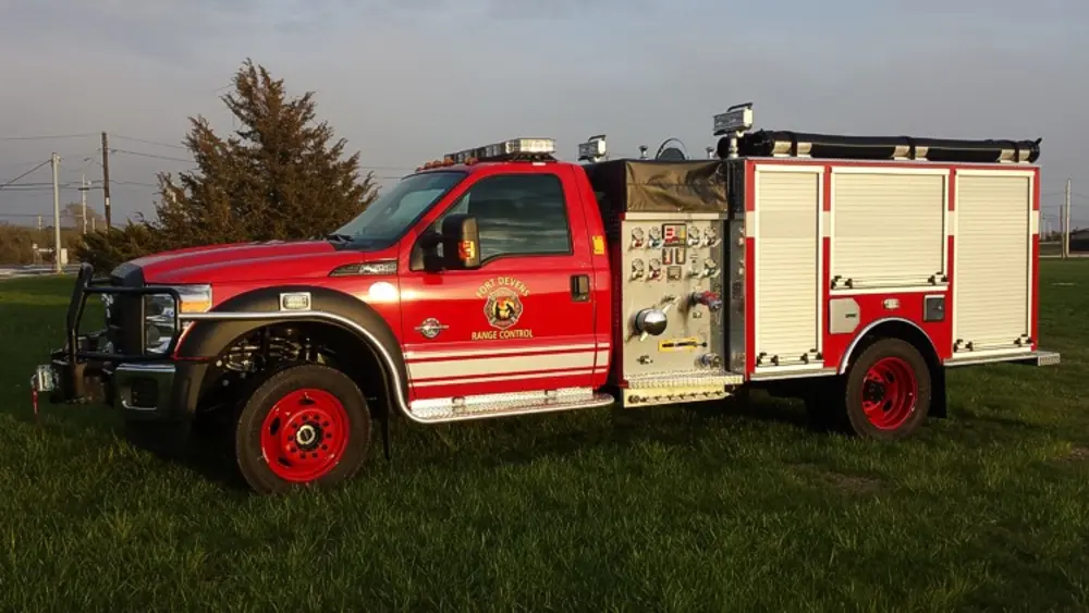 Exterior view of small fire truck showing cab, body compartments, and wheel/tire area.