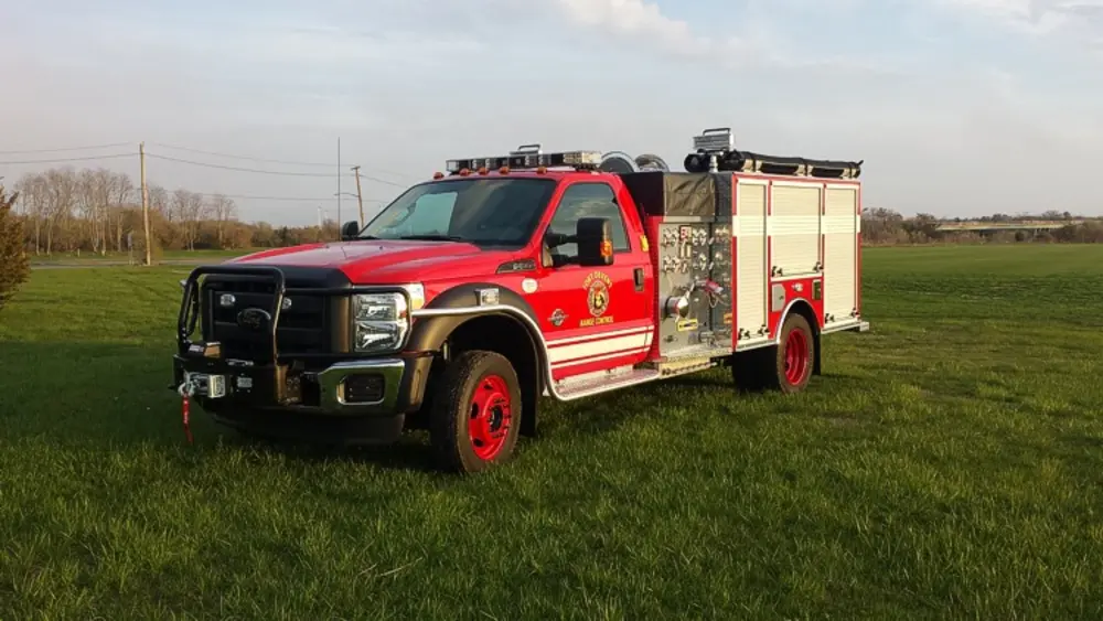 Exterior view of small fire truck showing cab, body compartments, and wheel/tire area.