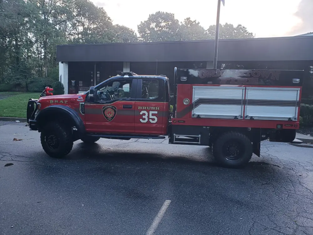 Exterior view of small fire truck showing cab, body compartments, and wheel/tire area.