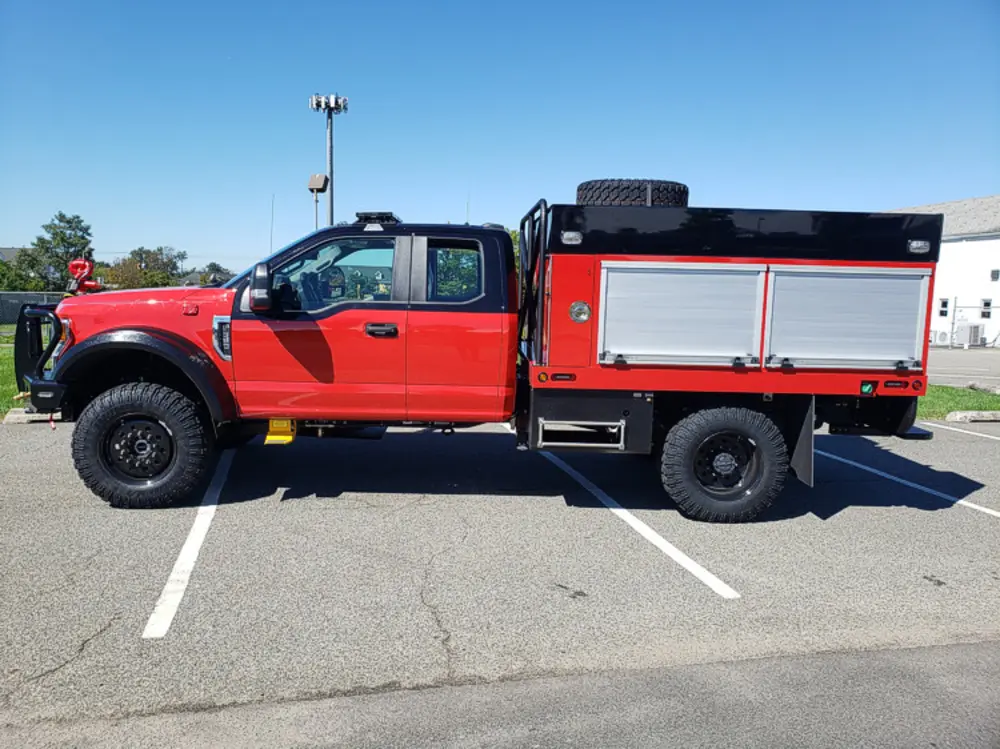 Exterior view of small fire truck showing cab, body compartments, and wheel/tire area.