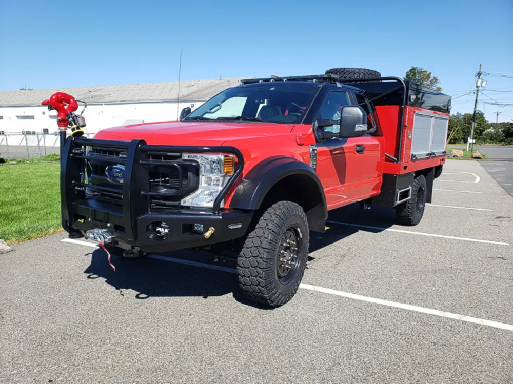 Exterior view of small fire truck showing cab, body compartments, and wheel/tire area.