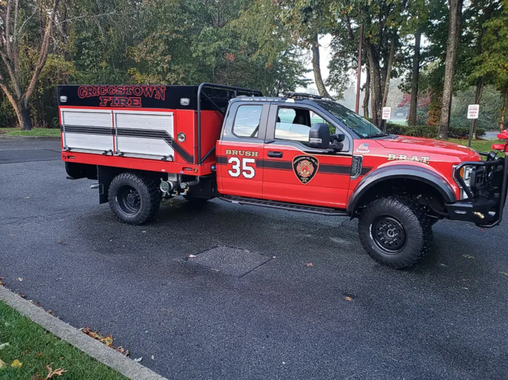 Exterior view of small fire truck showing cab, body compartments, and wheel/tire area.