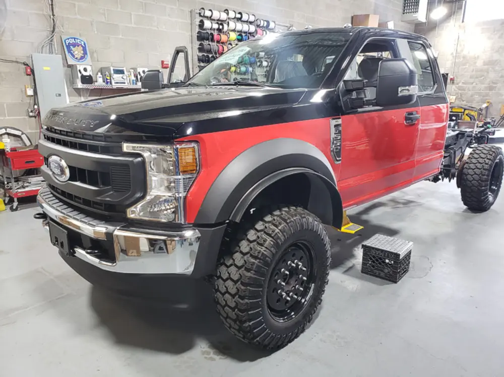 Exterior view of small fire truck showing cab, body compartments, and wheel/tire area.