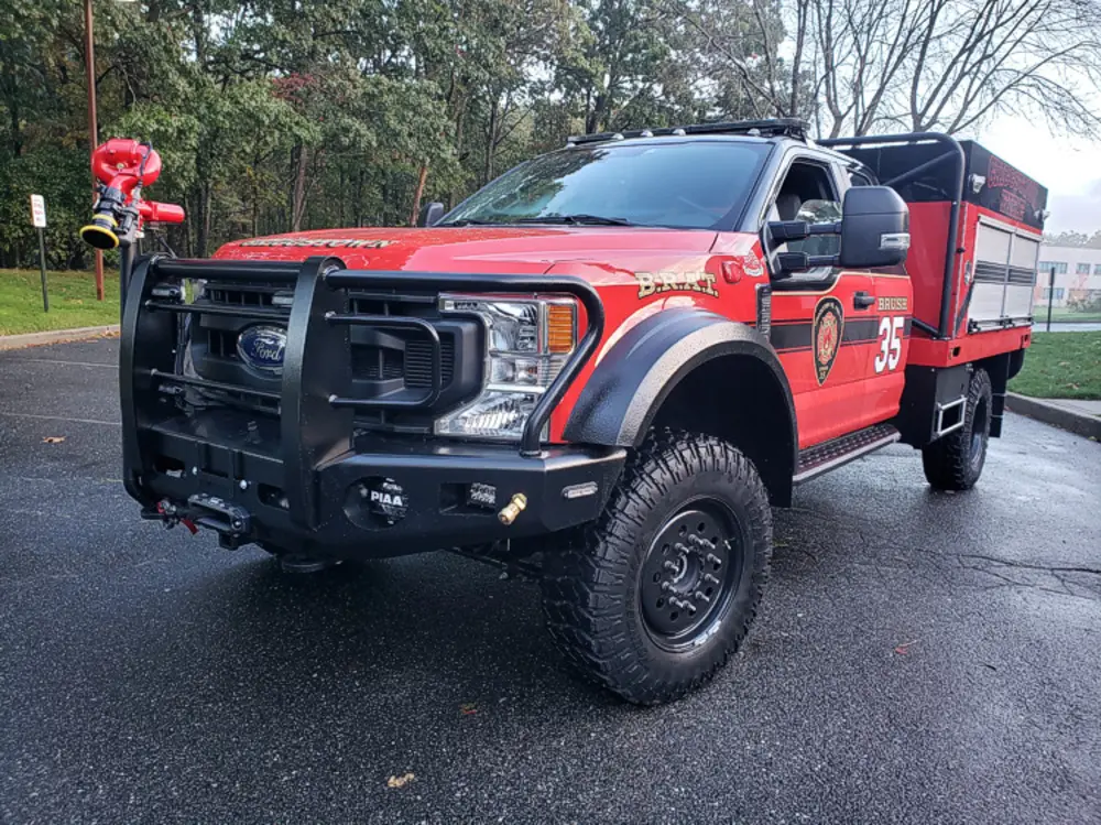 Exterior view of small fire truck showing cab, body compartments, and wheel/tire area.