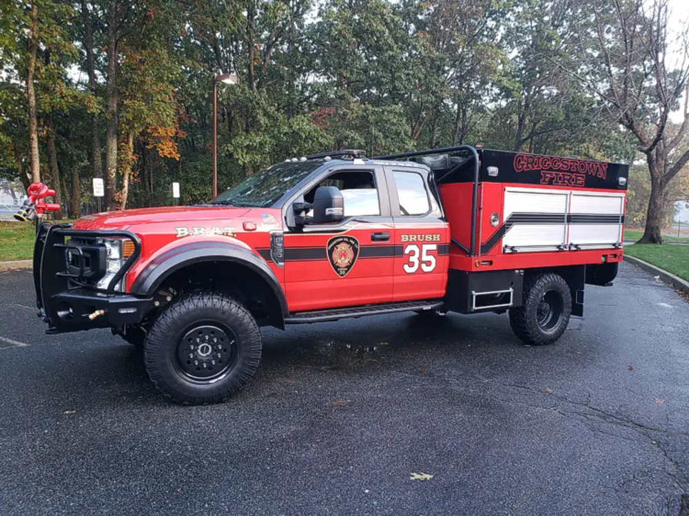 Exterior view of small fire truck showing cab, body compartments, and wheel/tire area.