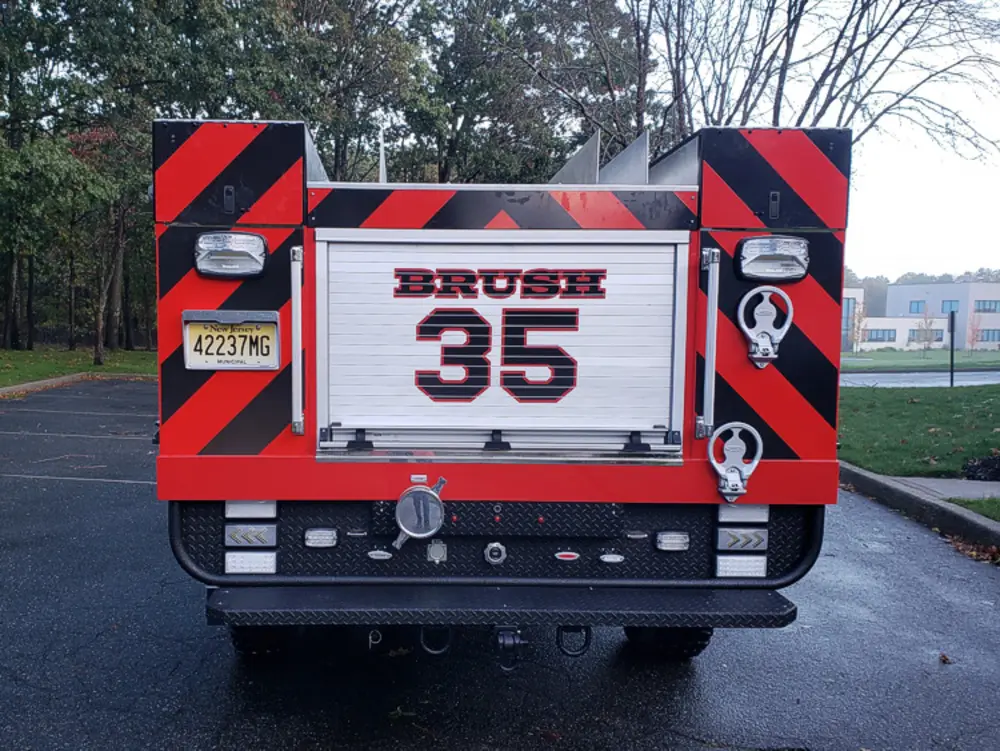Exterior view of small fire truck showing cab, body compartments, and wheel/tire area.