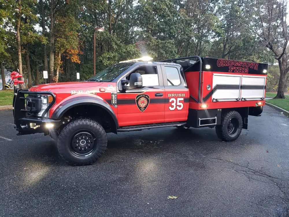 Exterior view of small fire truck showing cab, body compartments, and wheel/tire area.