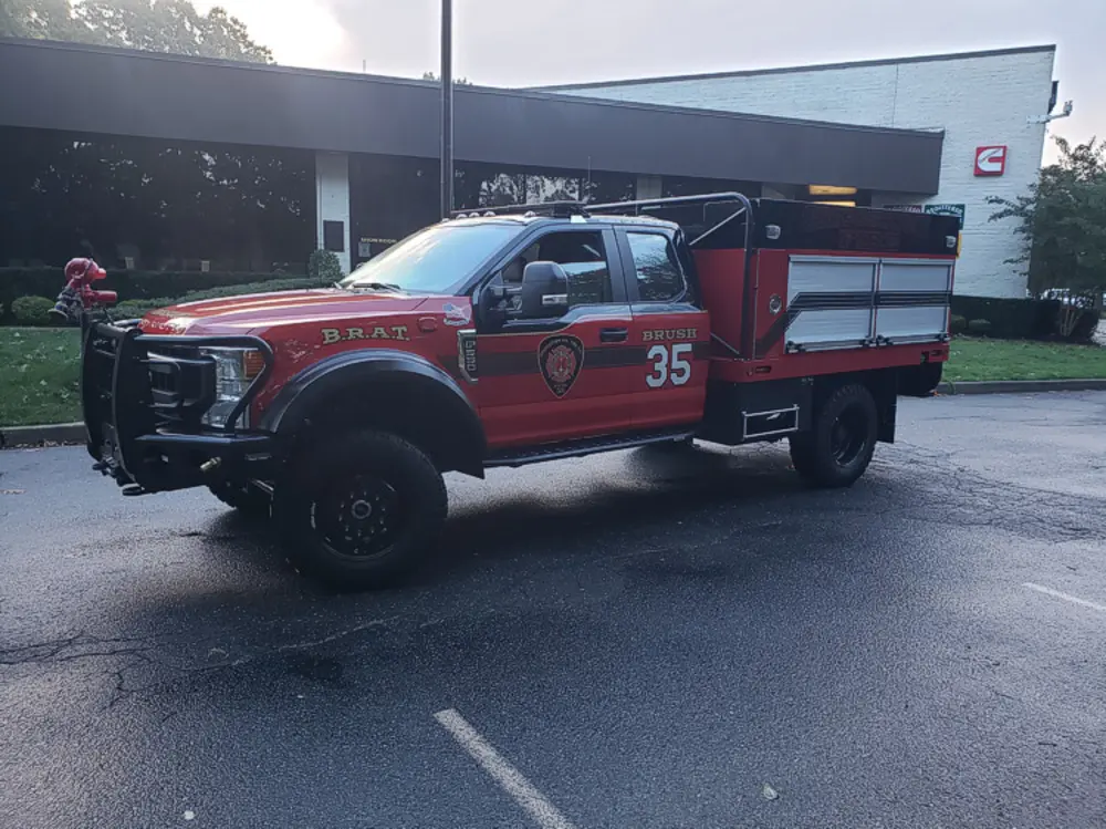 Exterior view of small fire truck showing cab, body compartments, and wheel/tire area.