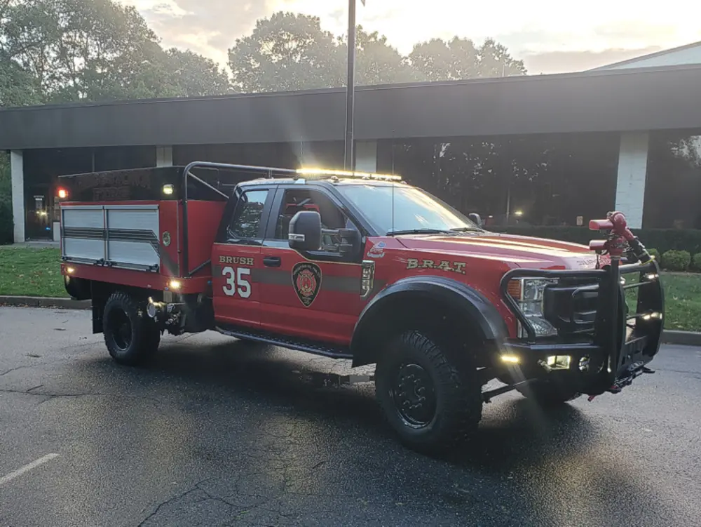 Exterior view of small fire truck showing cab, body compartments, and wheel/tire area.