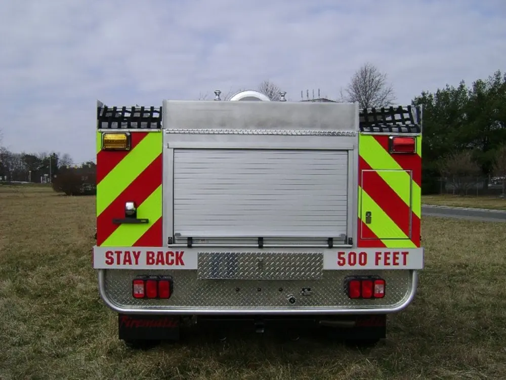 Exterior view of small fire truck showing cab, body compartments, and wheel/tire area.