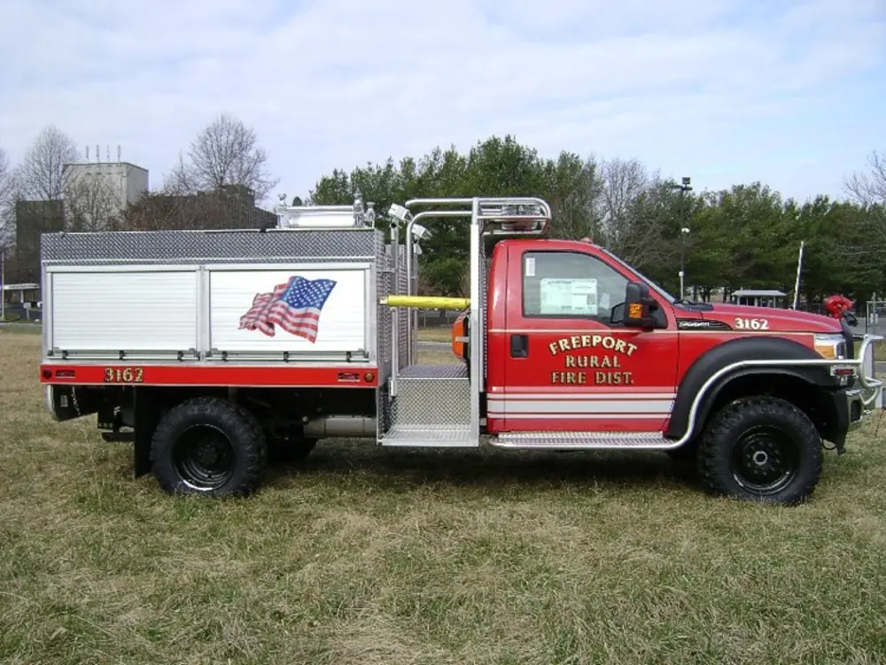 Exterior view of small fire truck showing cab, body compartments, and wheel/tire area.