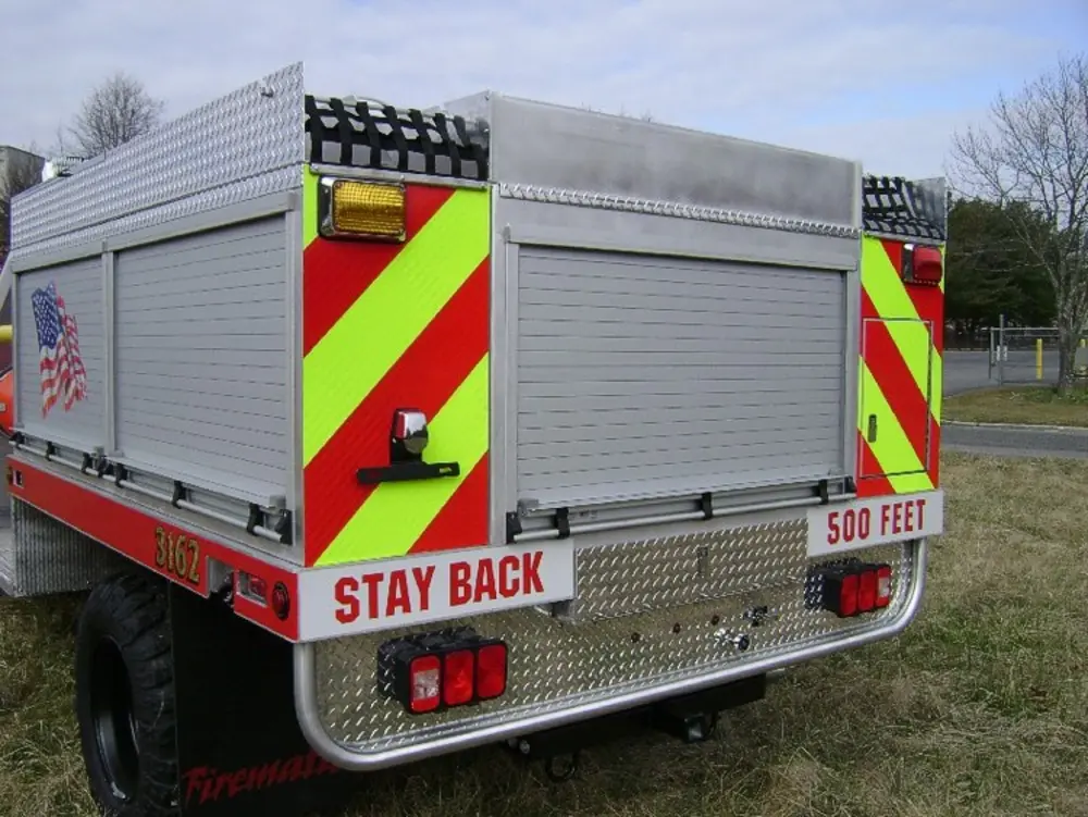 Exterior view of small fire truck showing cab, body compartments, and wheel/tire area.