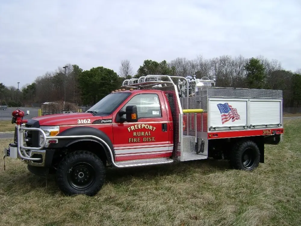 Exterior view of small fire truck showing cab, body compartments, and wheel/tire area.