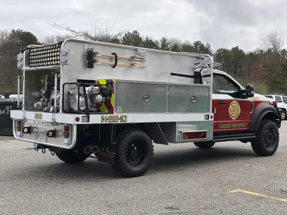 Exterior view of small fire truck showing cab, body compartments, and wheel/tire area.
