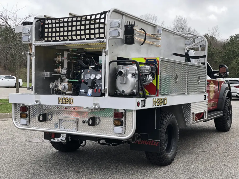 Exterior view of small fire truck showing cab, body compartments, and wheel/tire area.