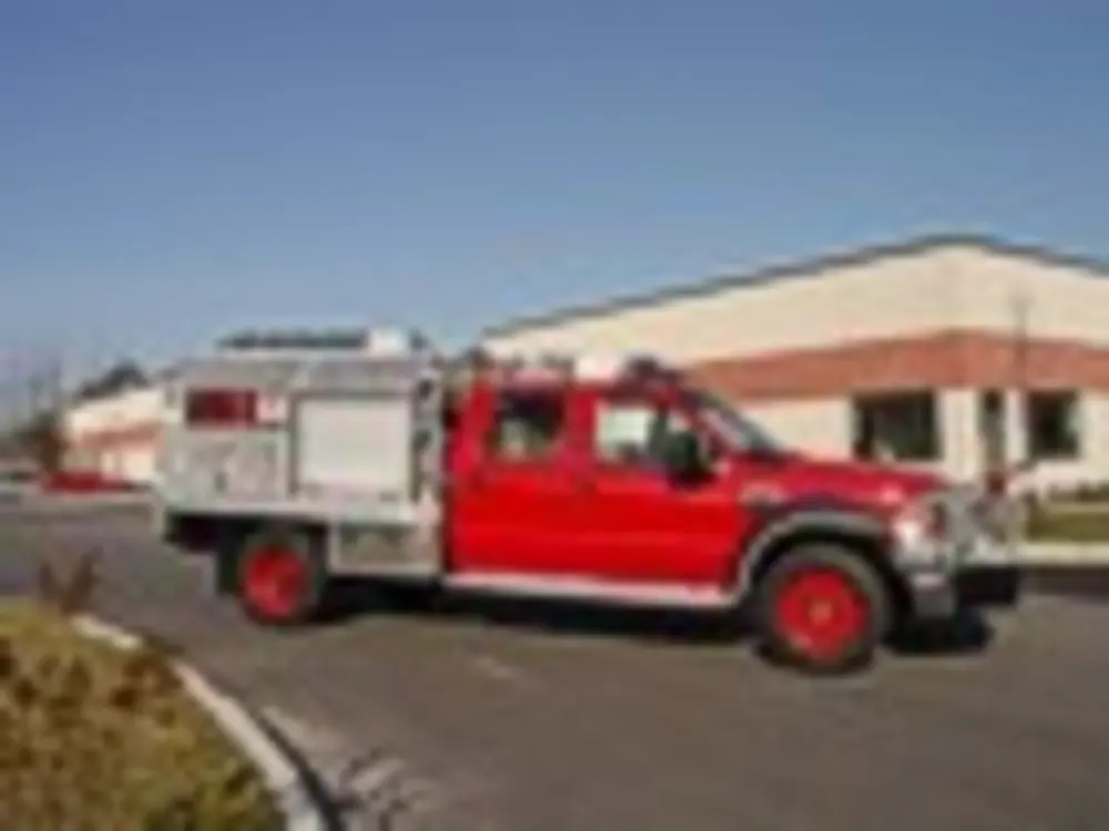 Exterior view of small fire truck showing cab, body compartments, and wheel/tire area.
