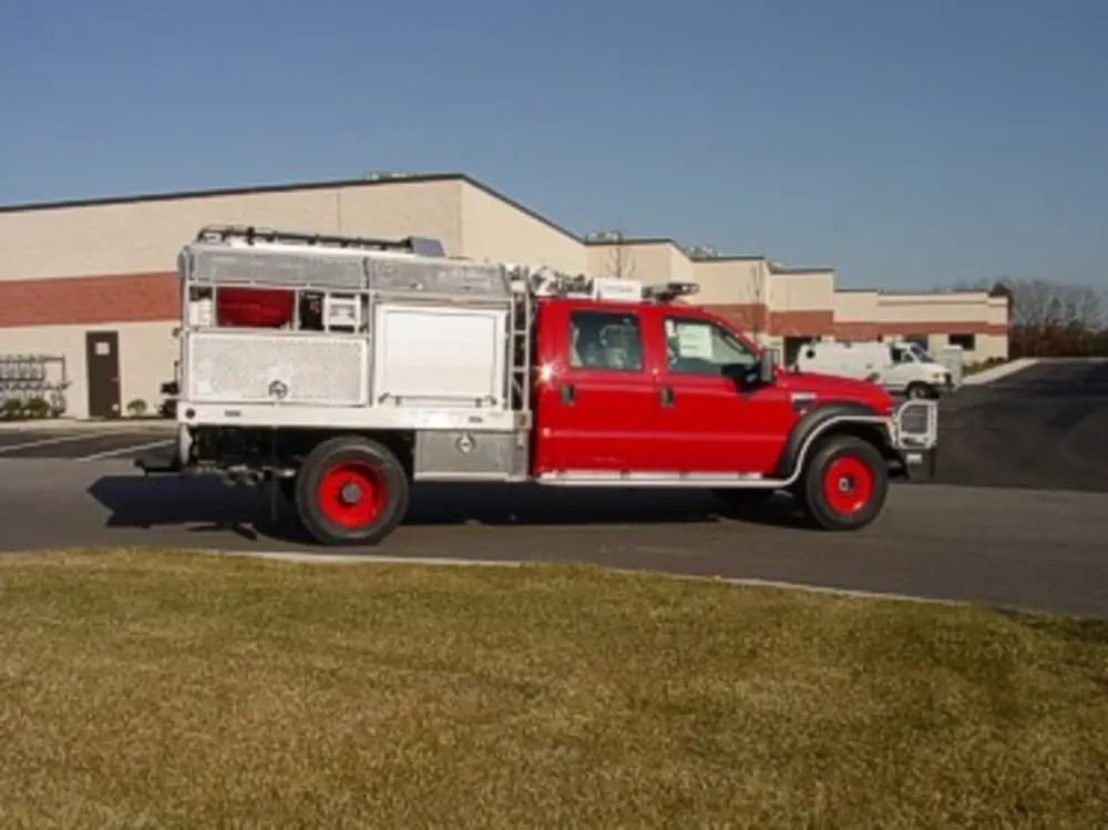 Exterior view of small fire truck showing cab, body compartments, and wheel/tire area.