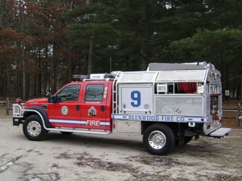 Exterior view of small fire truck showing cab, body compartments, and wheel/tire area.