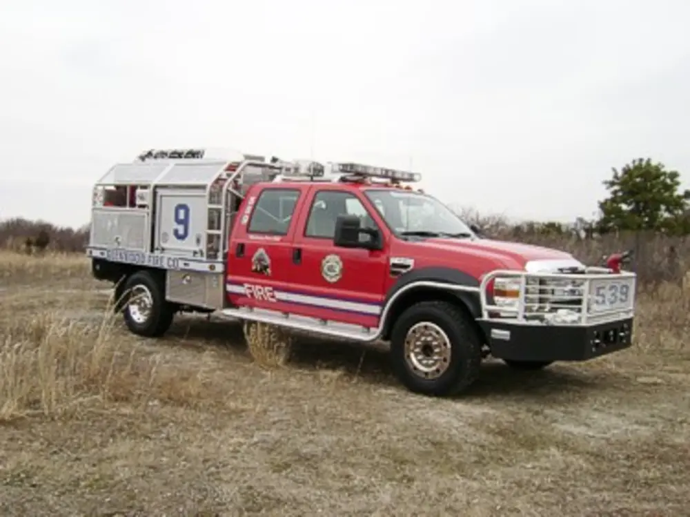 Exterior view of small fire truck showing cab, body compartments, and wheel/tire area.